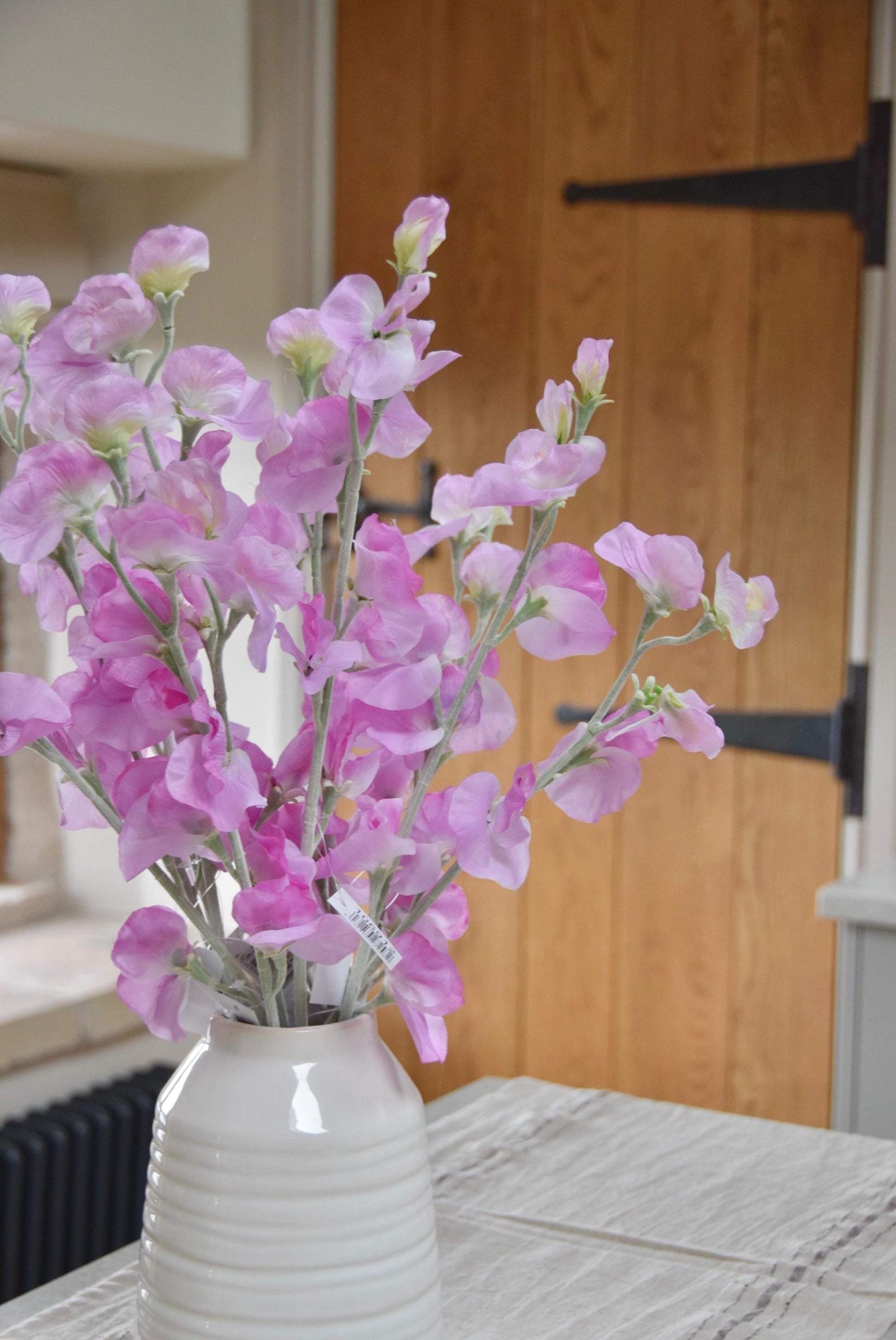Pink sweet peas set in a cream vase on a kitchen countertop in a country style house for home decor.