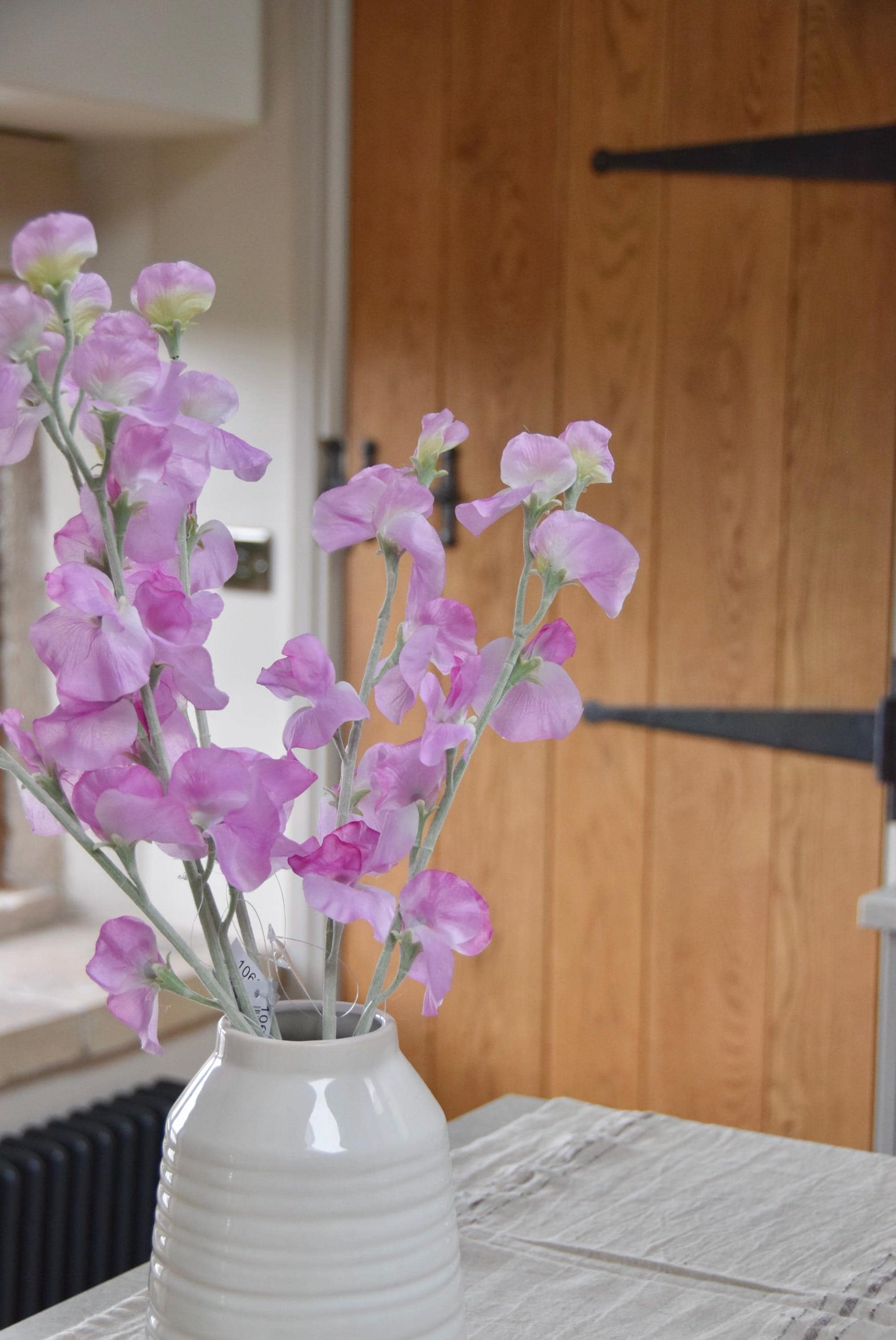 Pink sweet peas set in a cream vase on a kitchen countertop in a country style house for home decor.