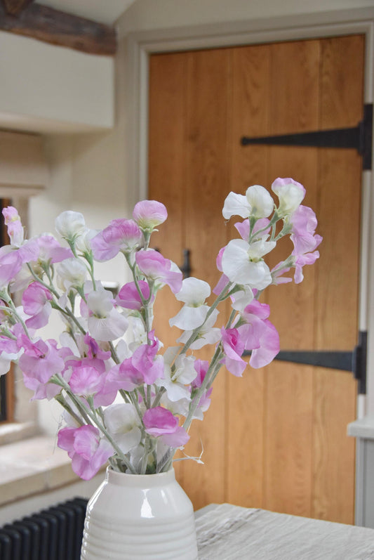 Pink and white sweet peas set in a cream vase on a kitchen countertop in a country style kitchen for home decor.