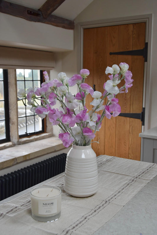 Pink and white sweet peas set in a cream vase on a kitchen countertop in a country style kitchen for home decor.