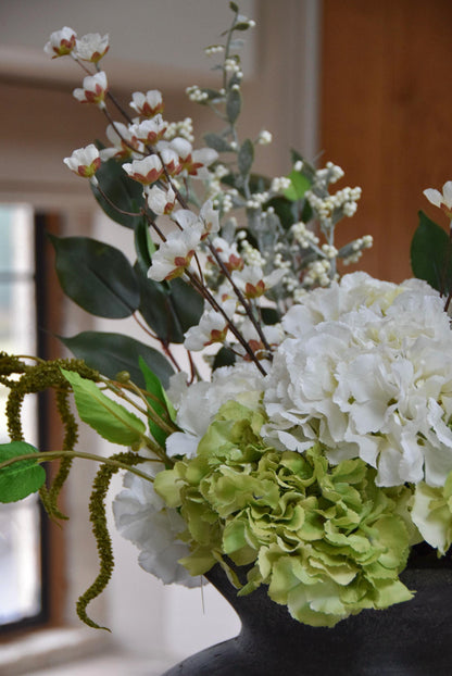 Grey vase placed on a kitchen countertop with a mixture of green and white hydrangeas with lots of mixed foliage. Displayed in a country style kitchen for home decor.
