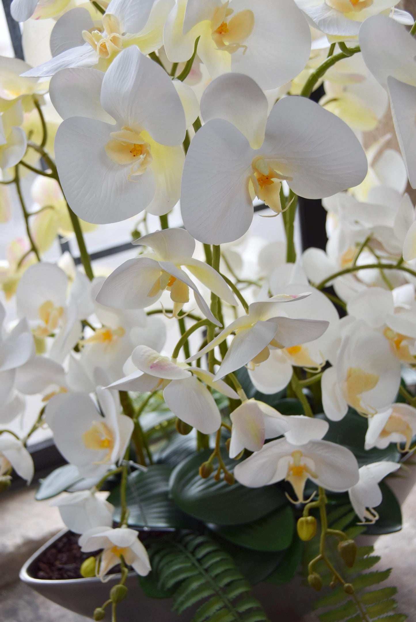 Silver ark bowl placed on a stone windowsill with an arrangement of white orchids. Arranged in a country style kitchen for home decor.