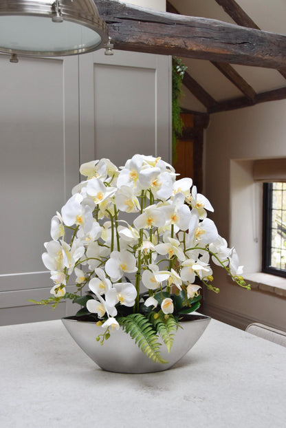 Silver ark bowl placed on a kitchen counter top with an arrangement of white orchids. Arranged in a country style kitchen for home decor.