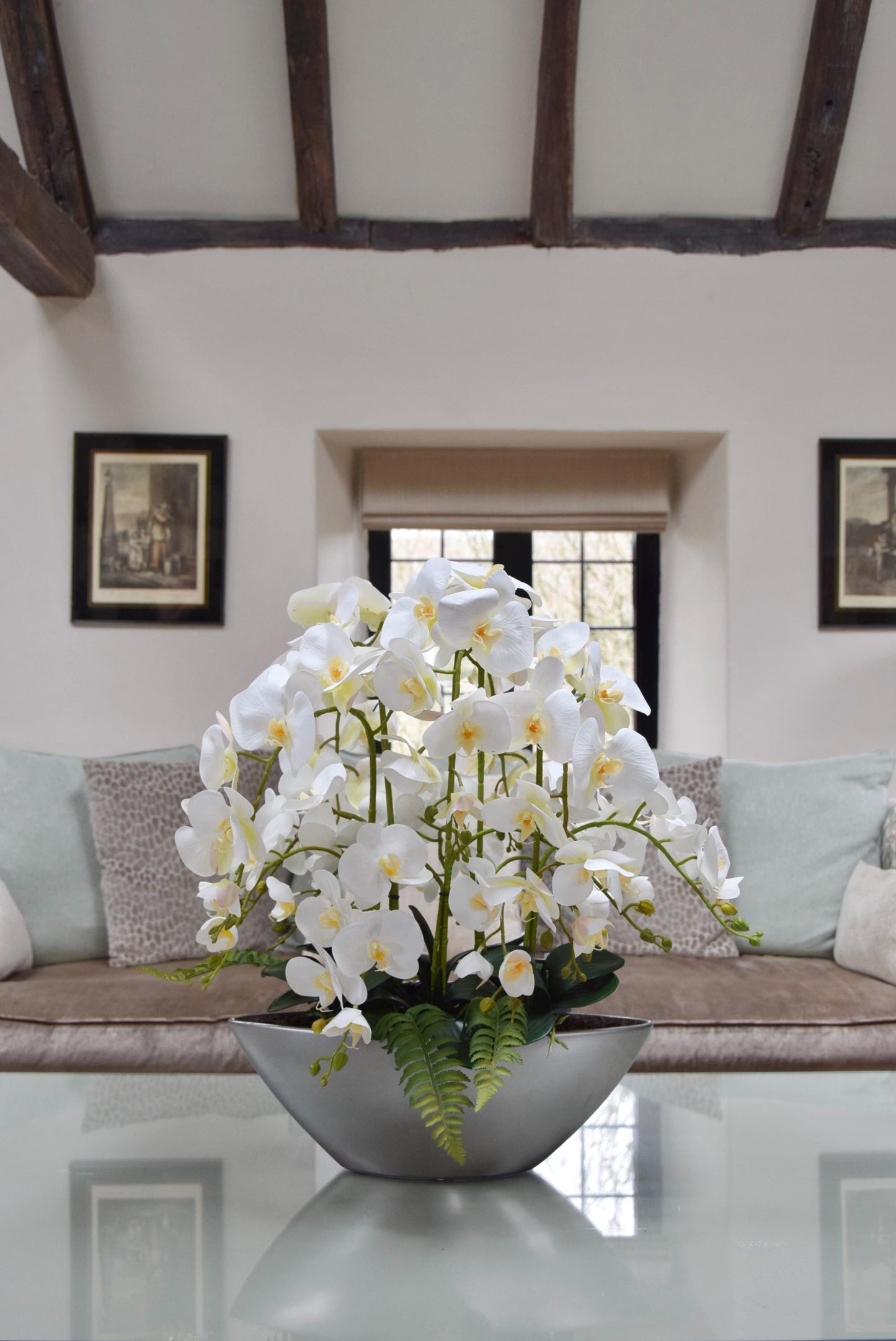 Silver ark bowl placed on a coffee table with an arrangement of white orchids. Arranged in a country style living room for home decor.