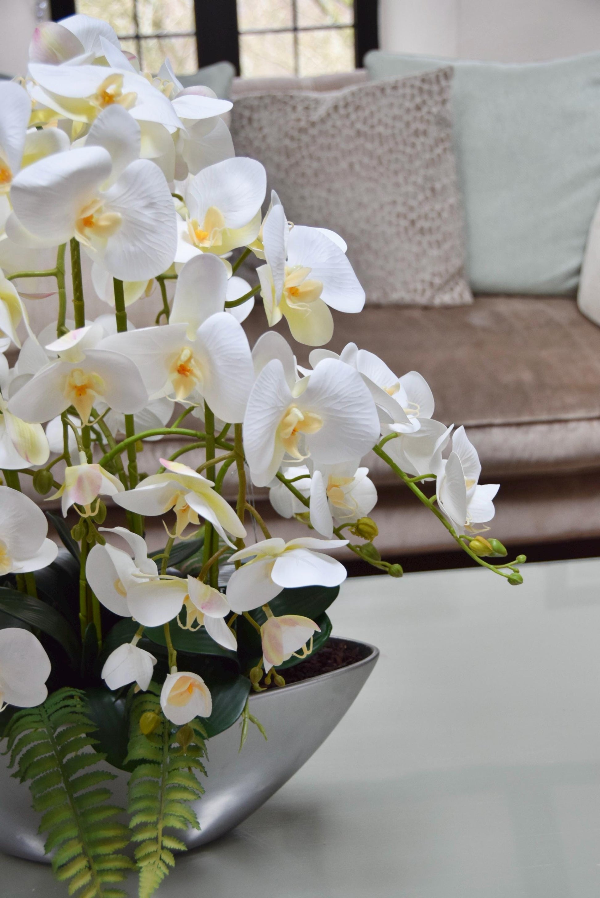 Silver ark bowl placed on a coffee table with an arrangement of white orchids. Arranged in a country style living room for home decor.