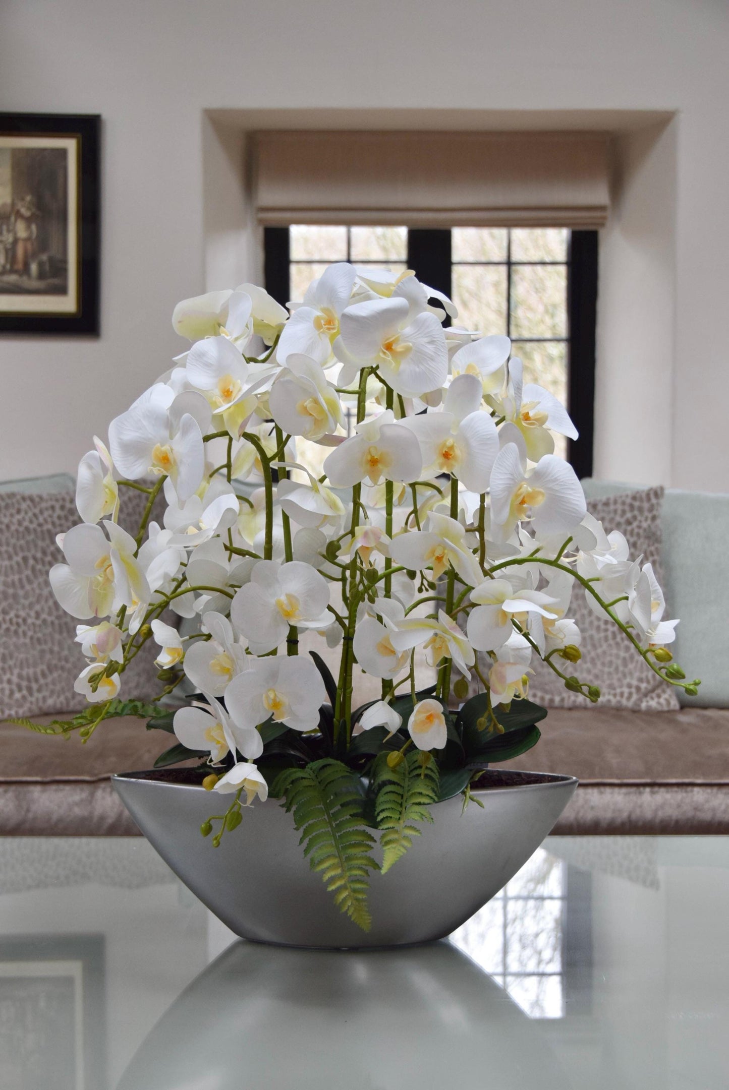 Silver ark bowl placed on a coffee table with an arrangement of white orchids. Arranged in a country style living room for home decor.