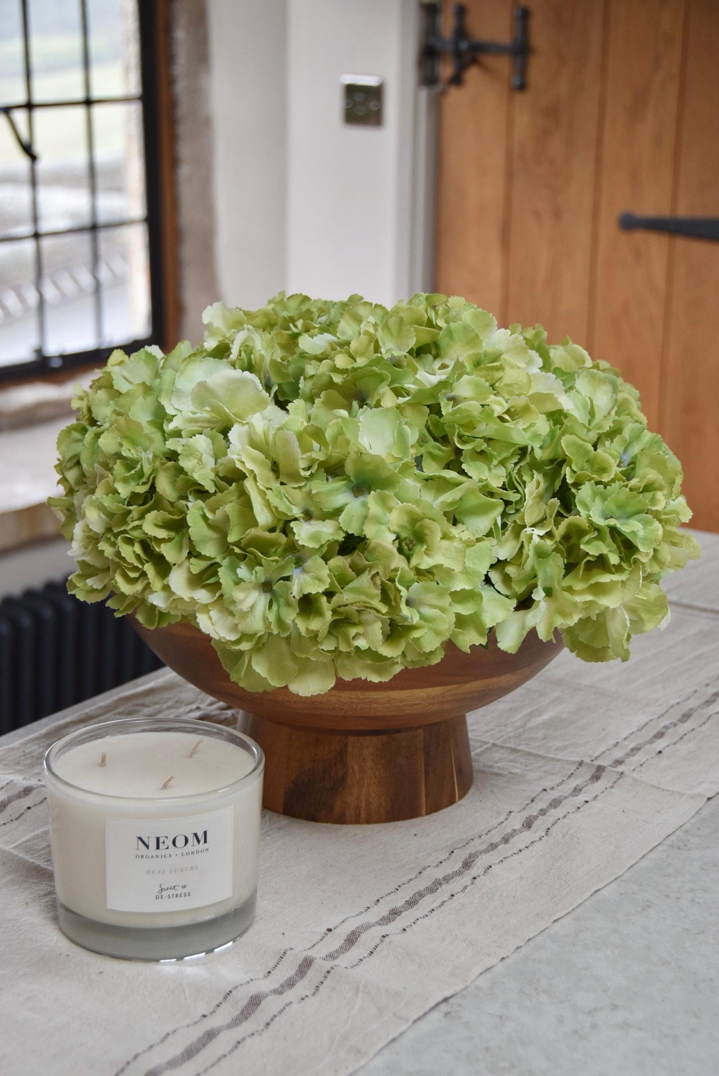 Wooden footed chalice bowl placed on a kitchen counter top with an arrangement of green hydrangeas. Displayed in a country style kitchen for home decor.