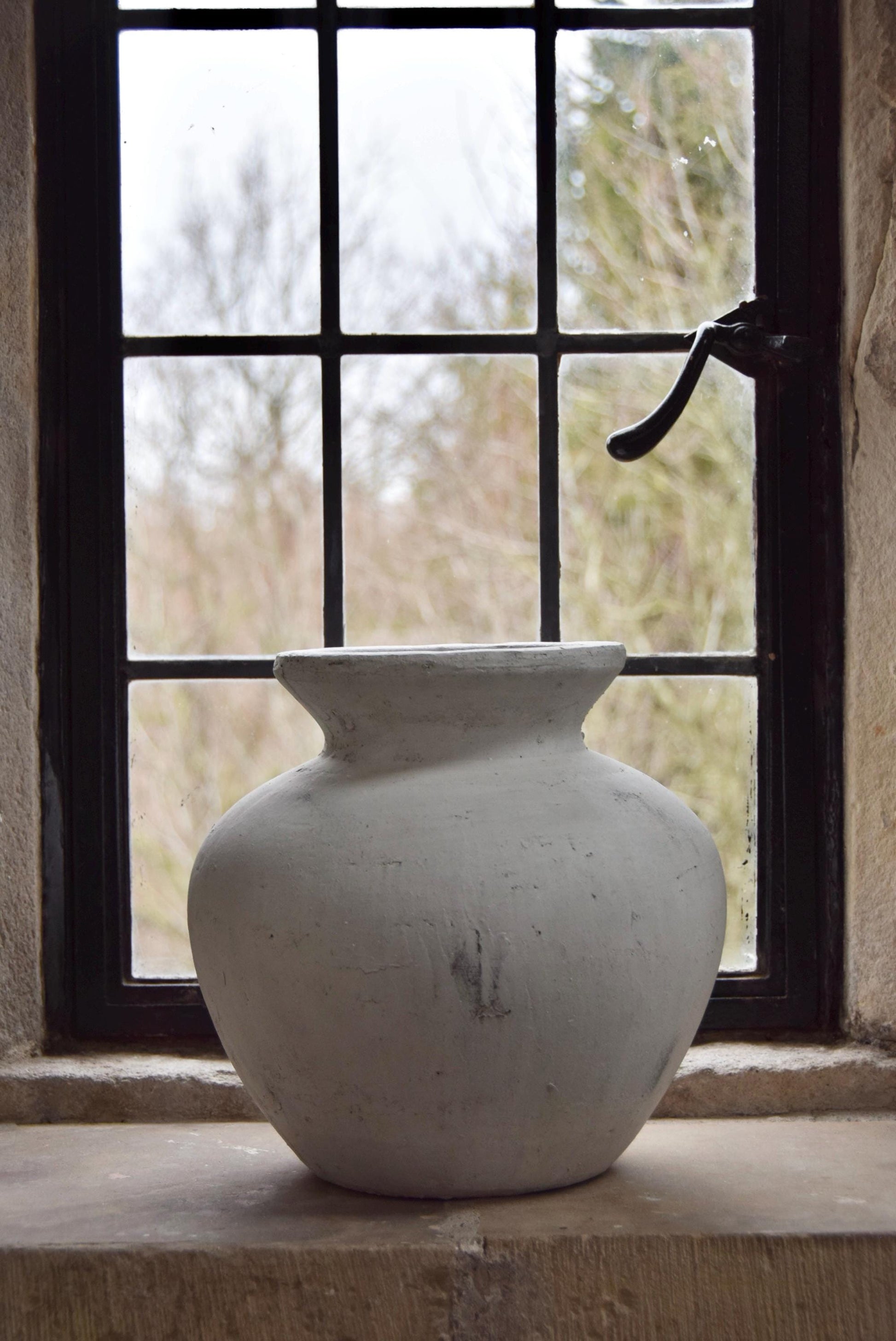 White stone vase placed on a stone windowsill. Displayed in a country style house for home decor.