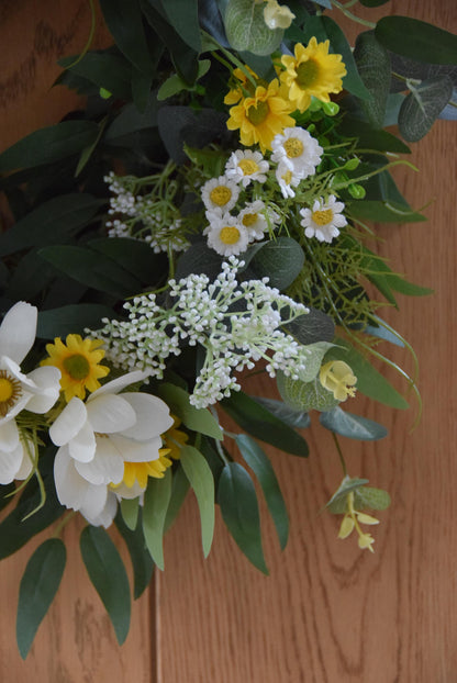 Wreath hanging on rustic country style wooden door with a mixture of daisies, wildflowers, mini bud sprays and greenery. Displayed on a barn door for home decor.