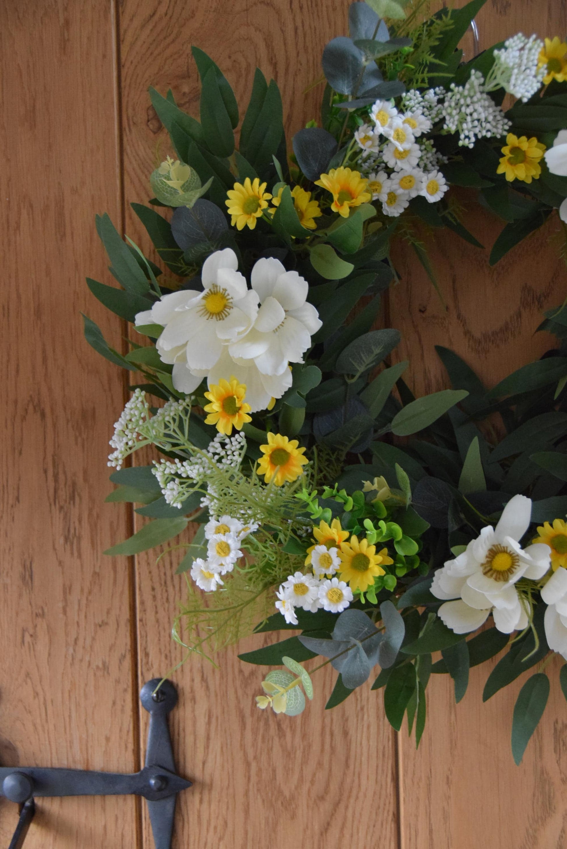Wreath hanging on rustic country style wooden door with a mixture of daisies, wildflowers, mini bud sprays and greenery. Displayed on a barn door for home decor.
