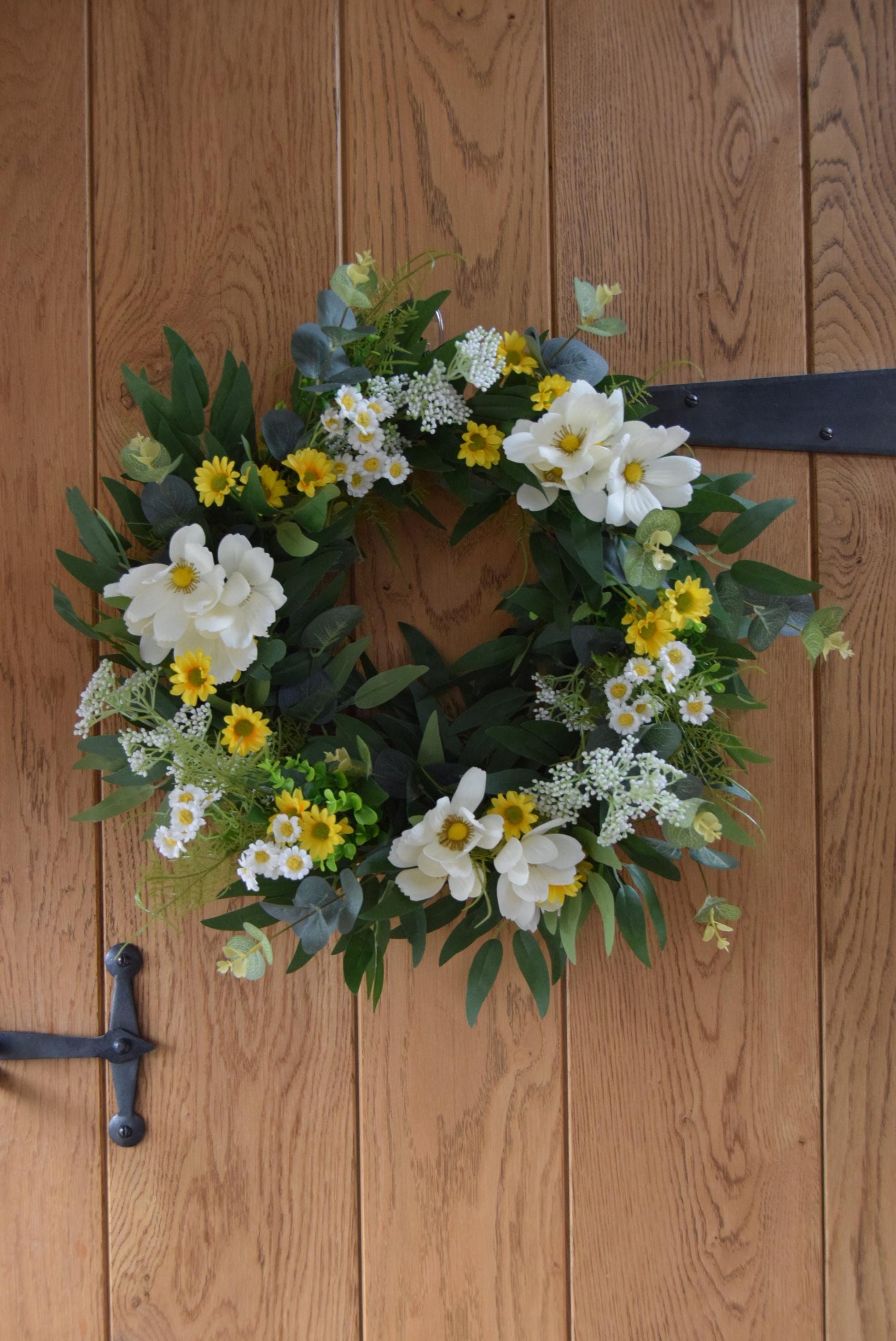 Wreath hanging on rustic country style wooden door with a mixture of daisies, wildflowers, mini bud sprays and greenery. Displayed on a barn door for home decor.