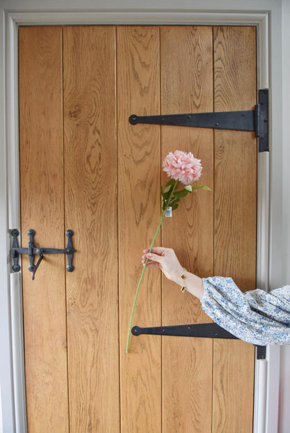 Artificial pink pom pom flower stem displayed against a country style wooden door.