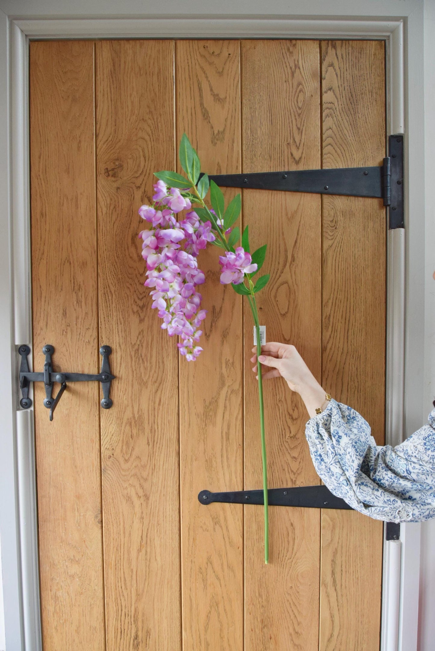 Tall artificial purple wisteria stem displayed against a country style wooden door.