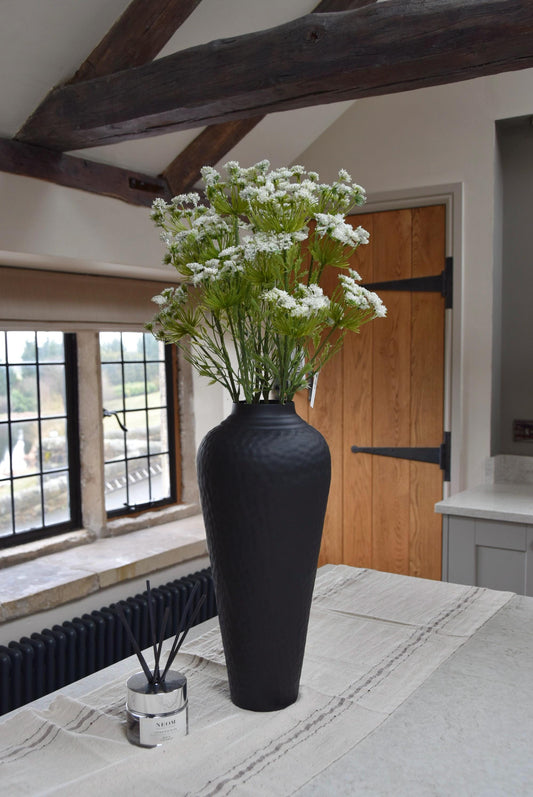 Tall black vase placed on a kitchen countertop with a bunch of white cow parsley. Displayed in a country style kitchen for home decor.