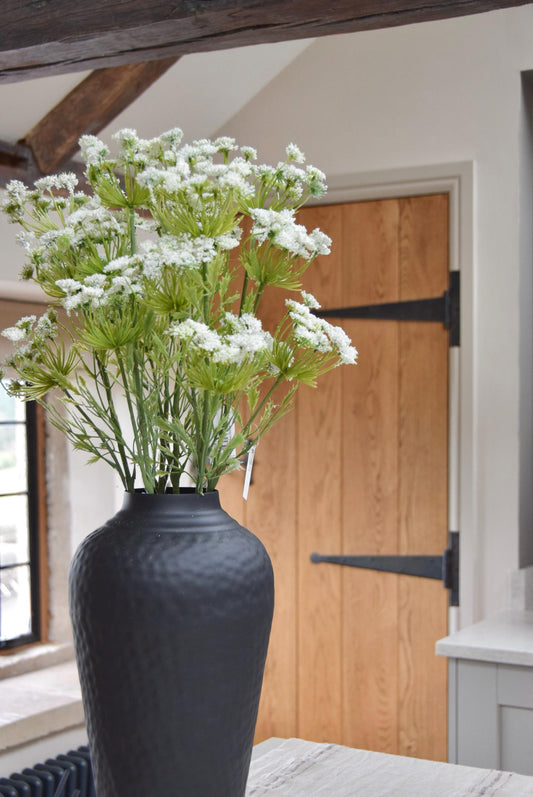 Tall black vase placed on a kitchen countertop with a bunch of white cow parsley. Displayed in a country style kitchen for home decor.