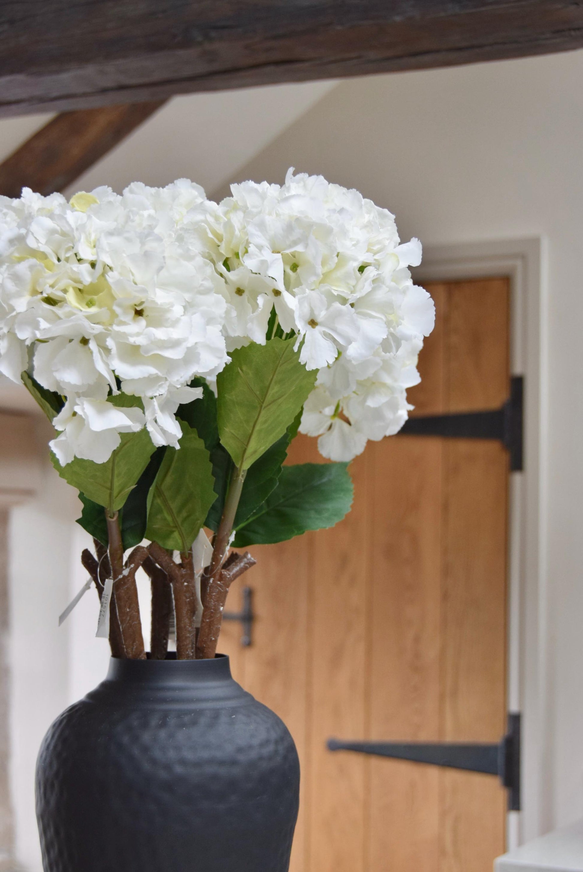 Tall black vase placed on a kitchen countertop with white hydrangeas. Displayed in a country style kitchen for home decor.