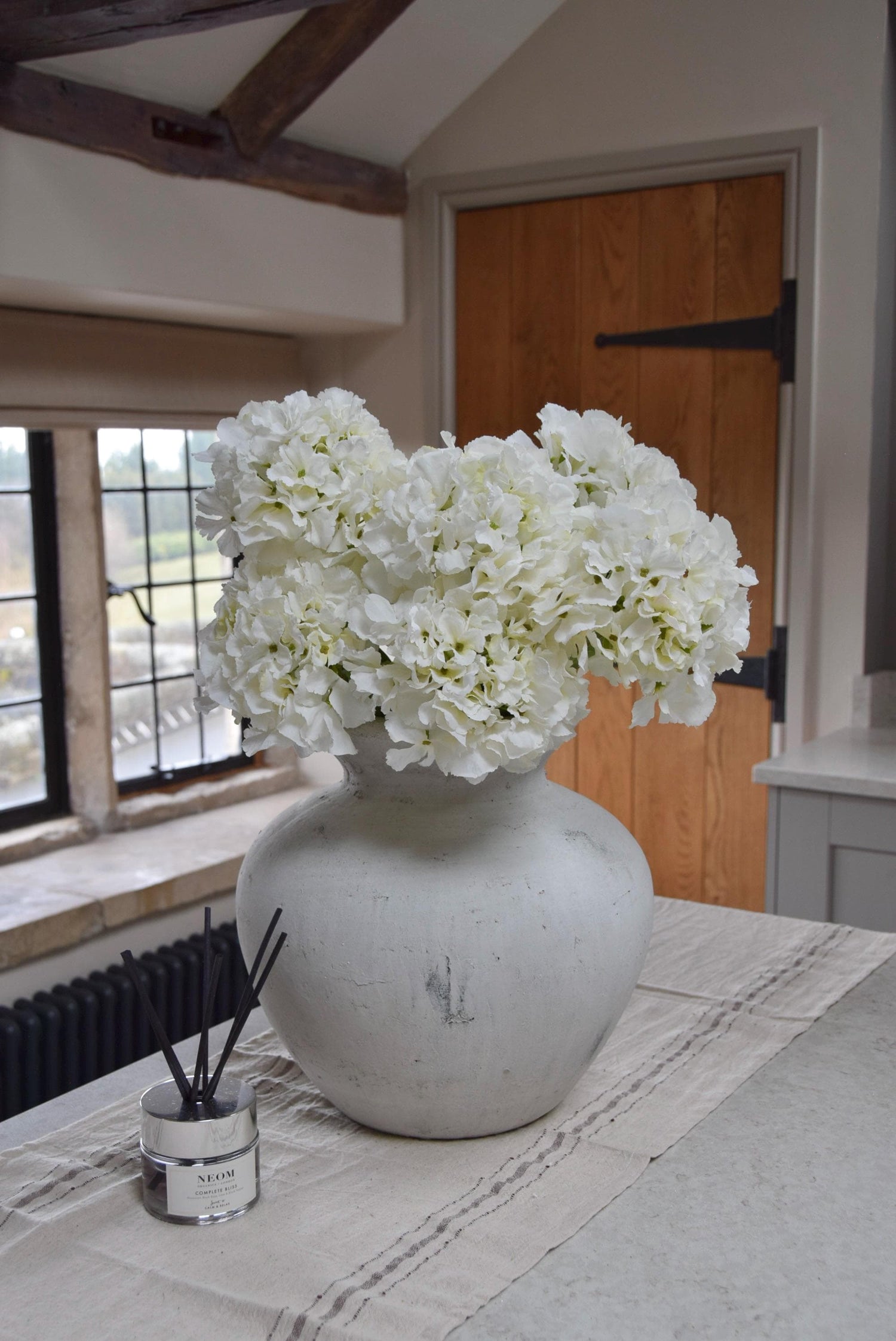 White stone vase on kitchen countertop featuring white hydrangeas. Displayed in a country style kitchen for home decor.