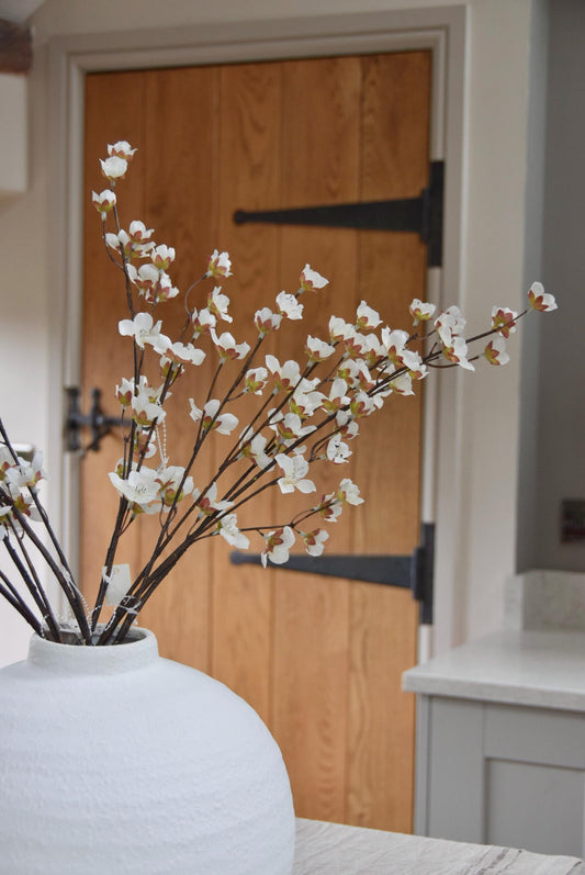 Round white vase placed on a kitchen countertop with a bunch of artificial cherry blossom branches. Displayed in a country style kitchen for home decor.