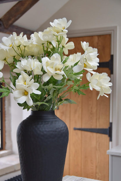 Tall black vase with cream wildflowers placed on a kitchen countertop in a country style kitchen for home decor.