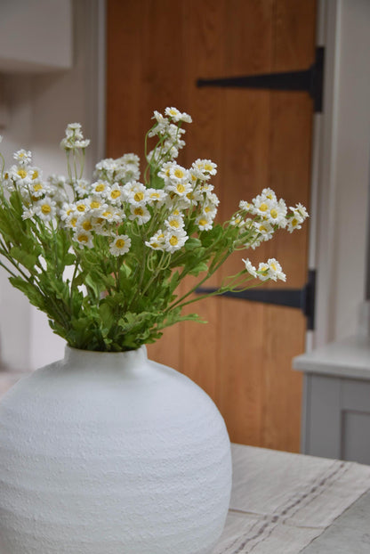 White round vase placed on a kitchen countertop with a bunch of daisies displayed in a country style kitchen for home decor.