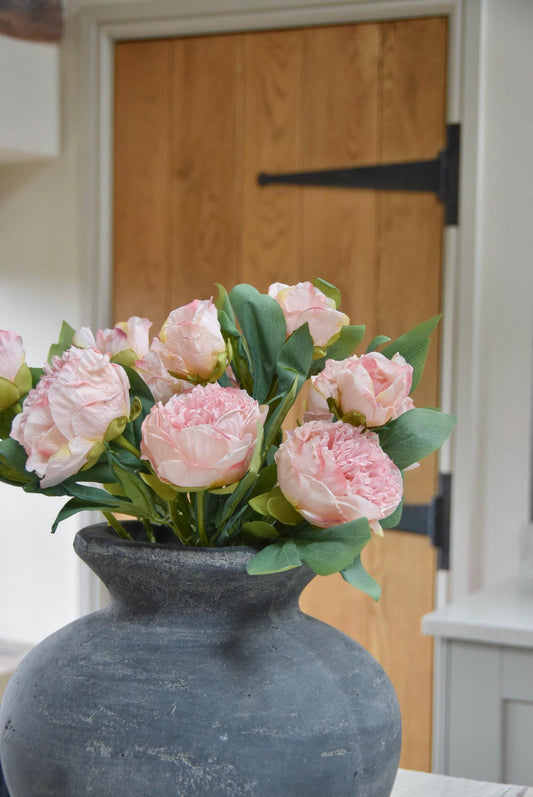 Grey vase placed on a kitchen countertop with a lovely bunch of pale pink peonies. Displayed in a country style kitchen for home decor.