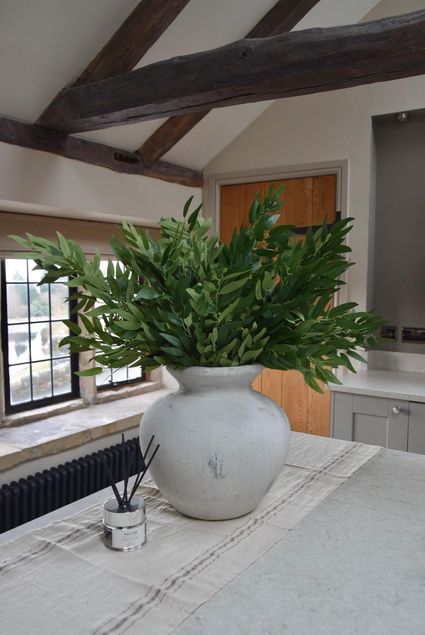 Stone vase on kitchen countertop featuring green foliage leaf stems in a country style kitchen for home decor.