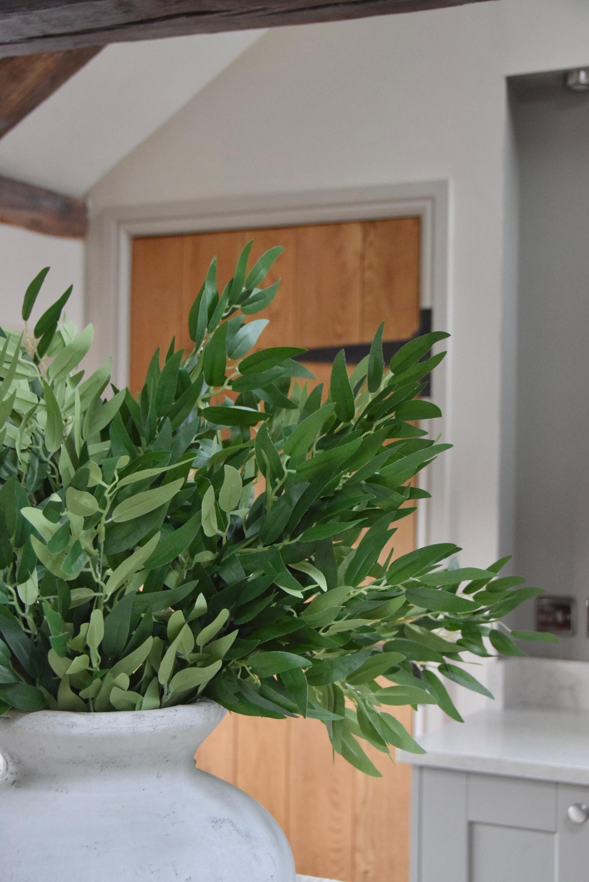 Stone vase on kitchen countertop featuring green foliage leaf stems in a country style kitchen for home decor.