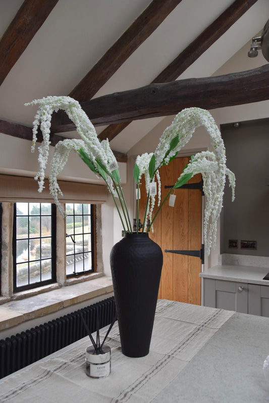 Tall black vase on a kitchen countertop with long white amaranthus trailing stems. Set in a country style kitchen for home decor.