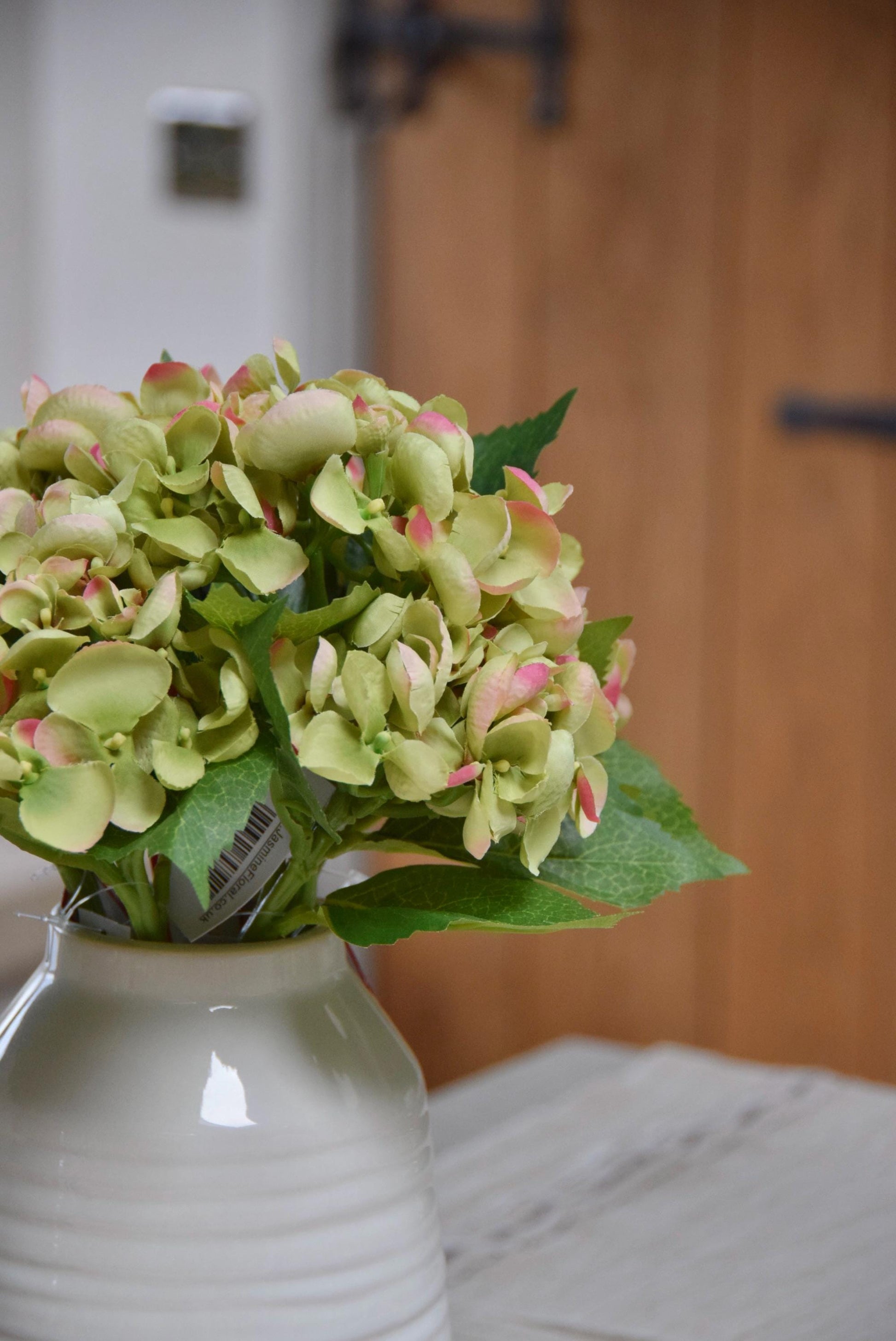 Mini green Hydrangeas in a small cream vase sat on a kitchen countertop in a country style house for home decor.