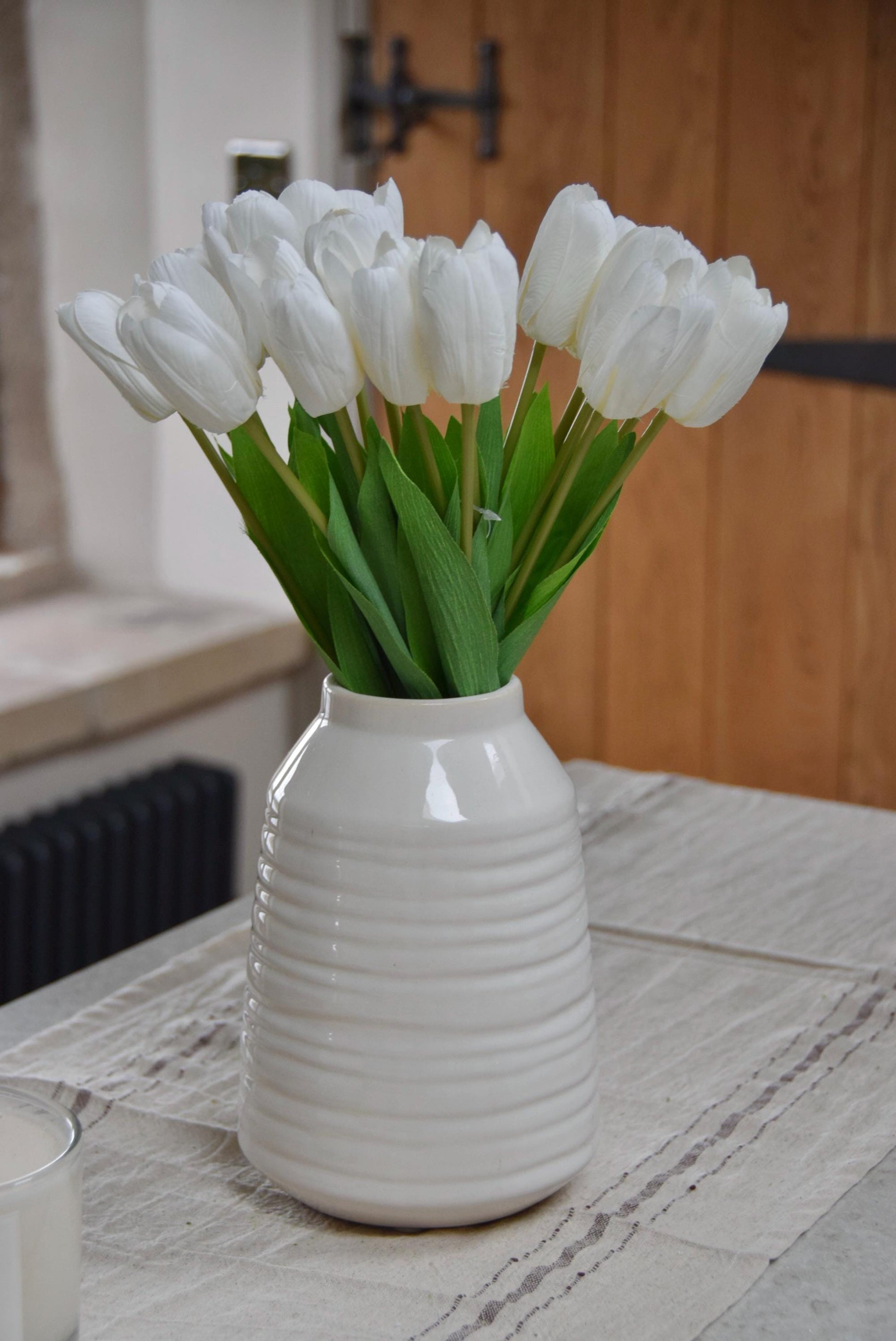 White tulips set in a cream vase on a kitchen counter top in a country style kitchen for home decor
