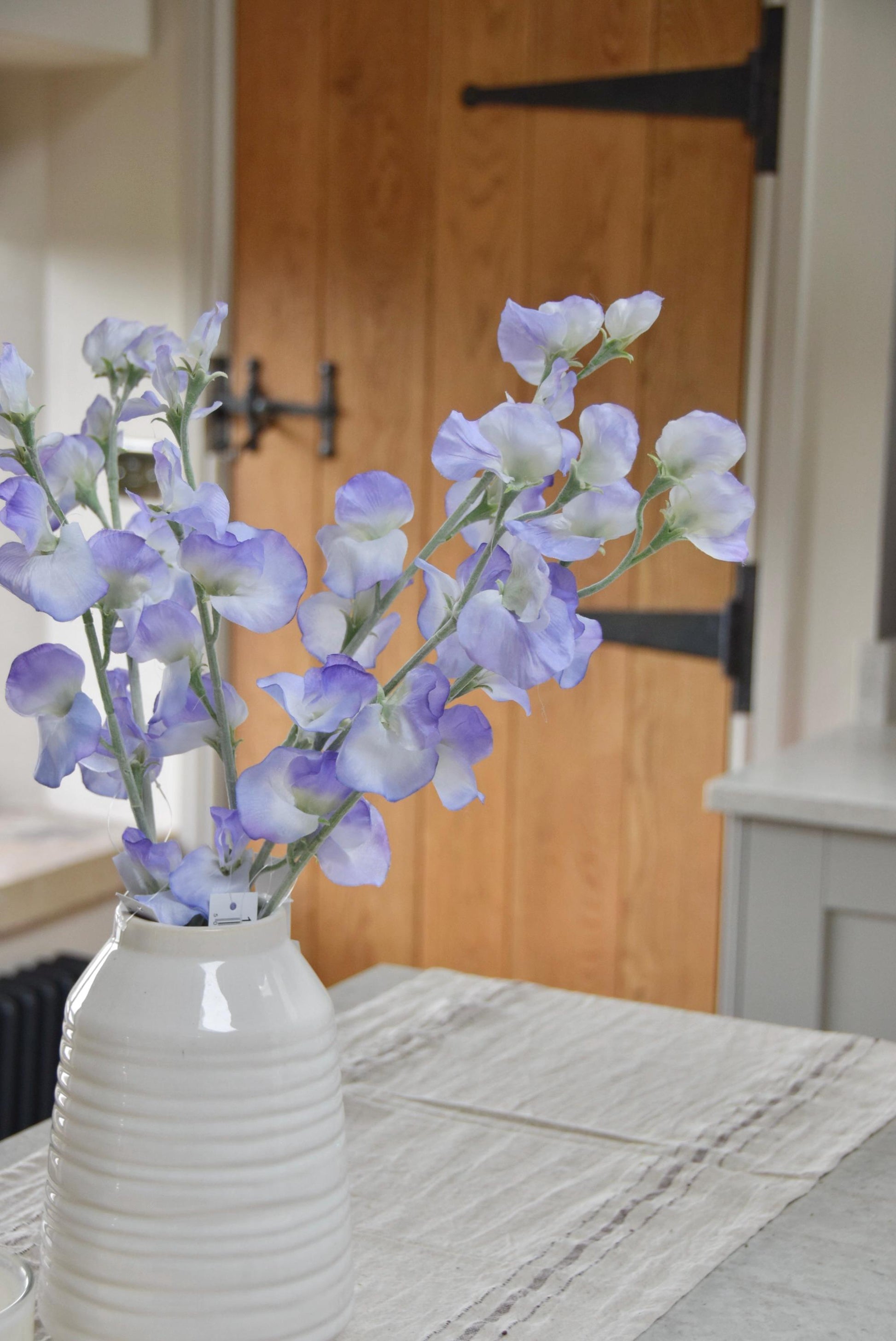 Lilac sweet peas set in a cream vase on a kitchen countertop in a country style house for home decor.