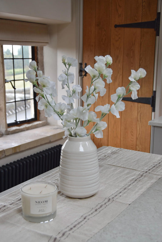 White sweet peas set in a cream vase on a kitchen countertop in a country style house for home decor.