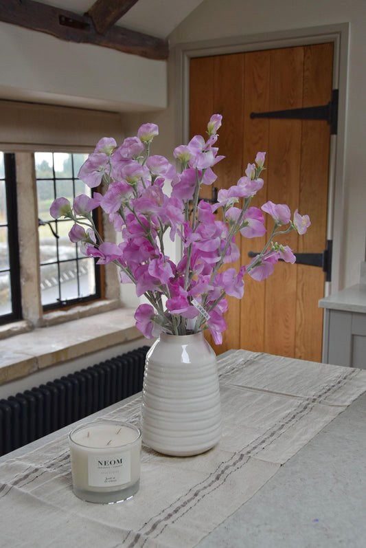 Pink sweet peas set in a cream vase on a kitchen countertop in a country style house for home decor.
