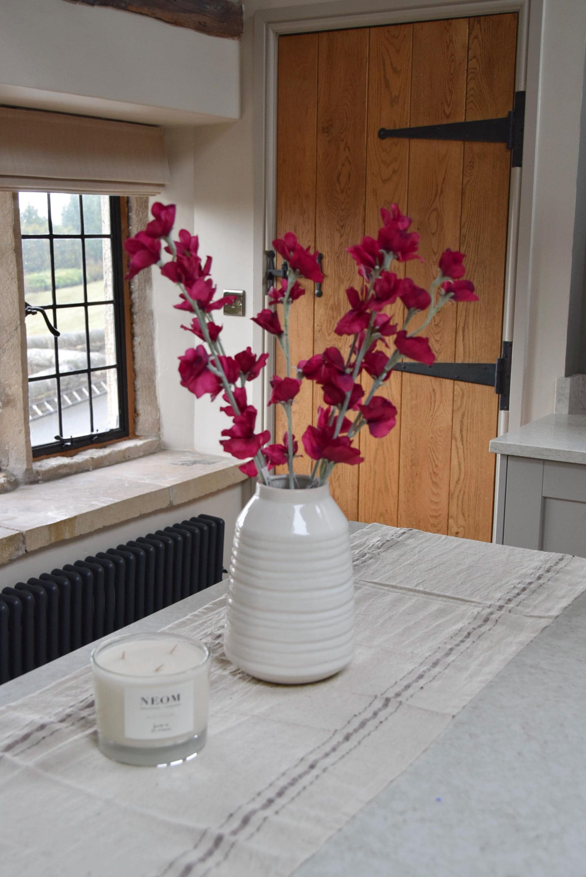 Red sweet peas set in a cream vase on a kitchen countertop in a country style house for home decor.