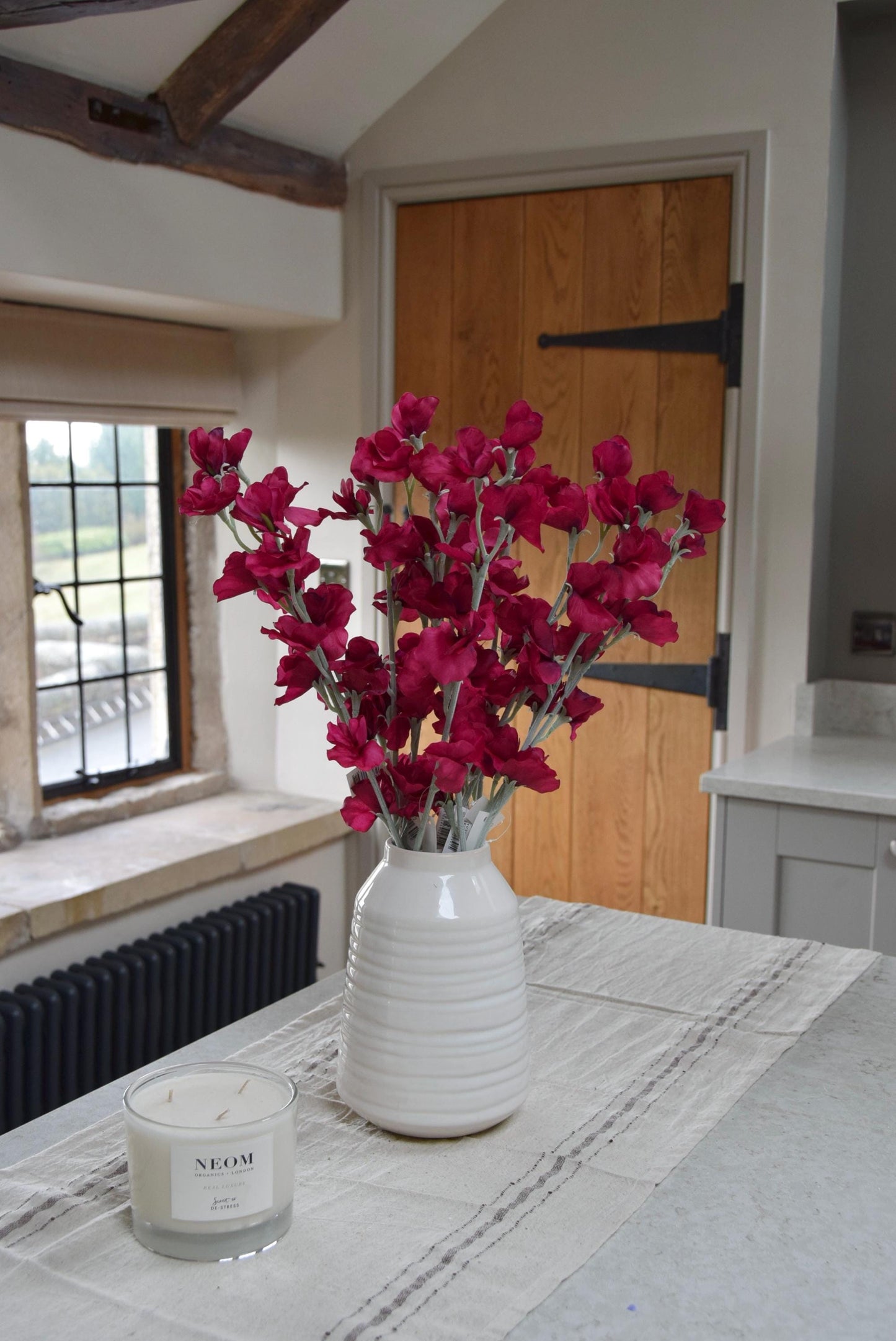 Red sweet peas set in a cream vase on a kitchen countertop in a country style house for home decor.