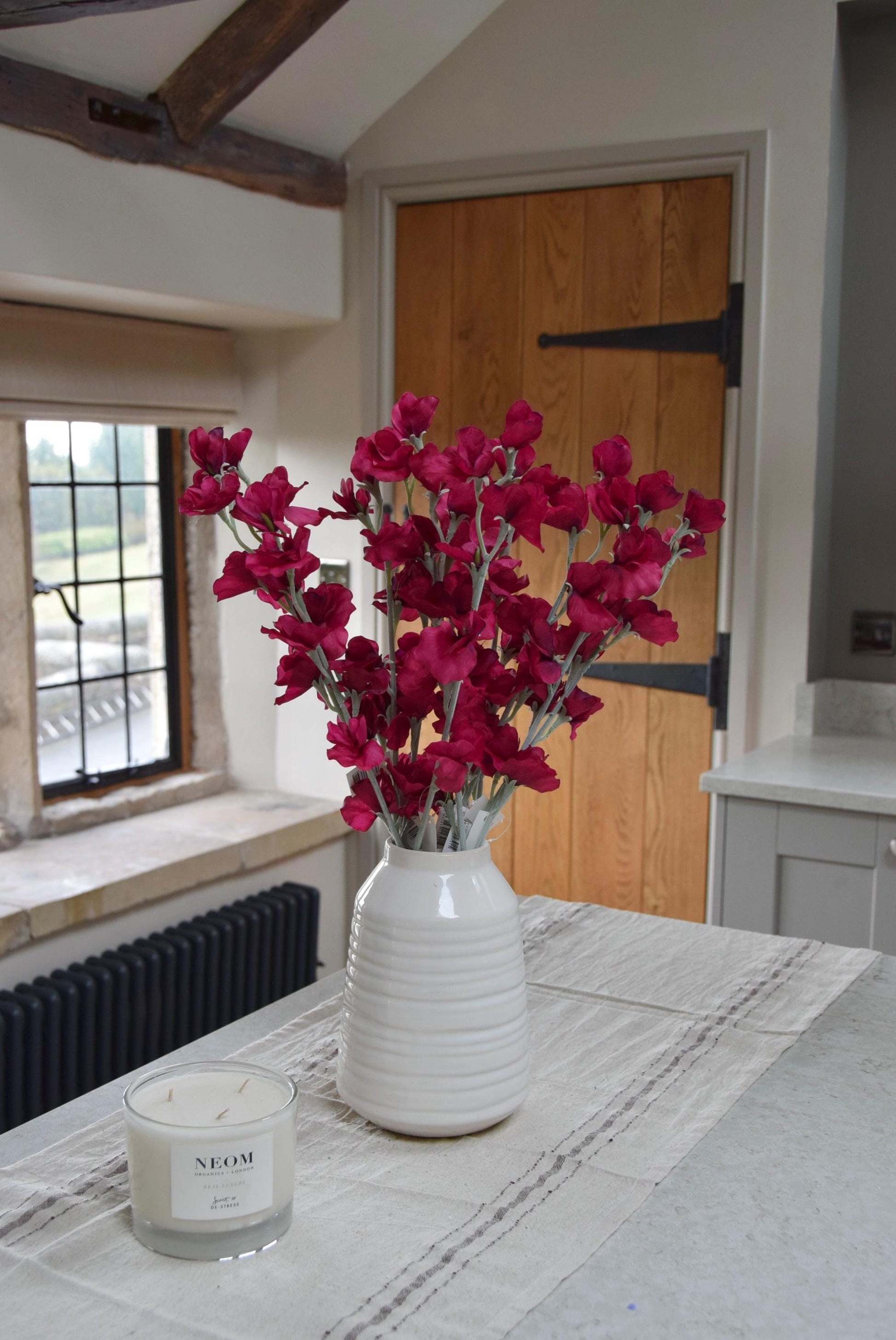 Red sweet peas set in a cream vase on a kitchen countertop in a country style house for home decor.