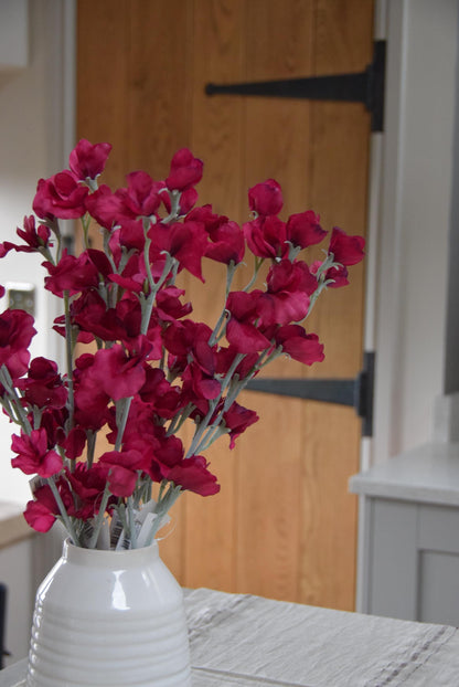 Red sweet peas set in a cream vase on a kitchen countertop in a country style house for home decor.