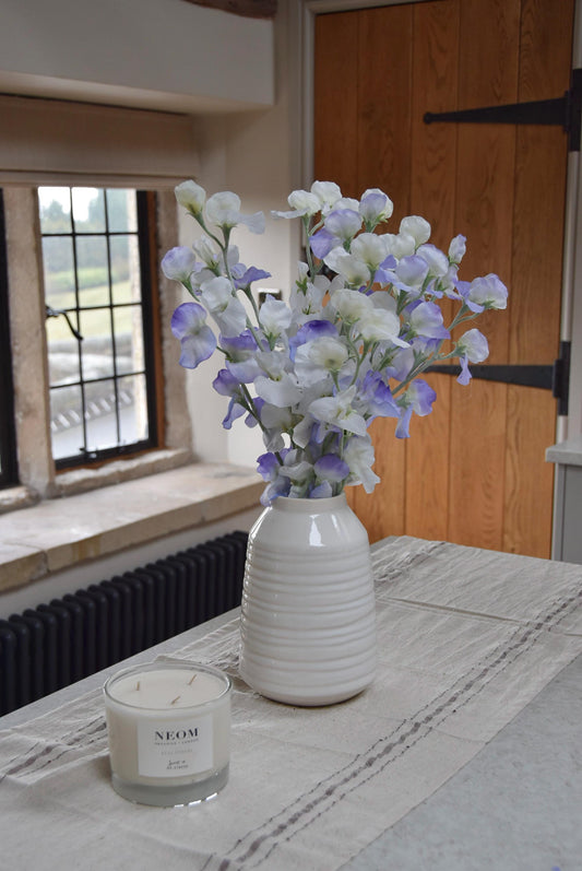 Lilac and white sweet peas set in a cream vase on a kitchen countertop in a country style kitchen for home decor.