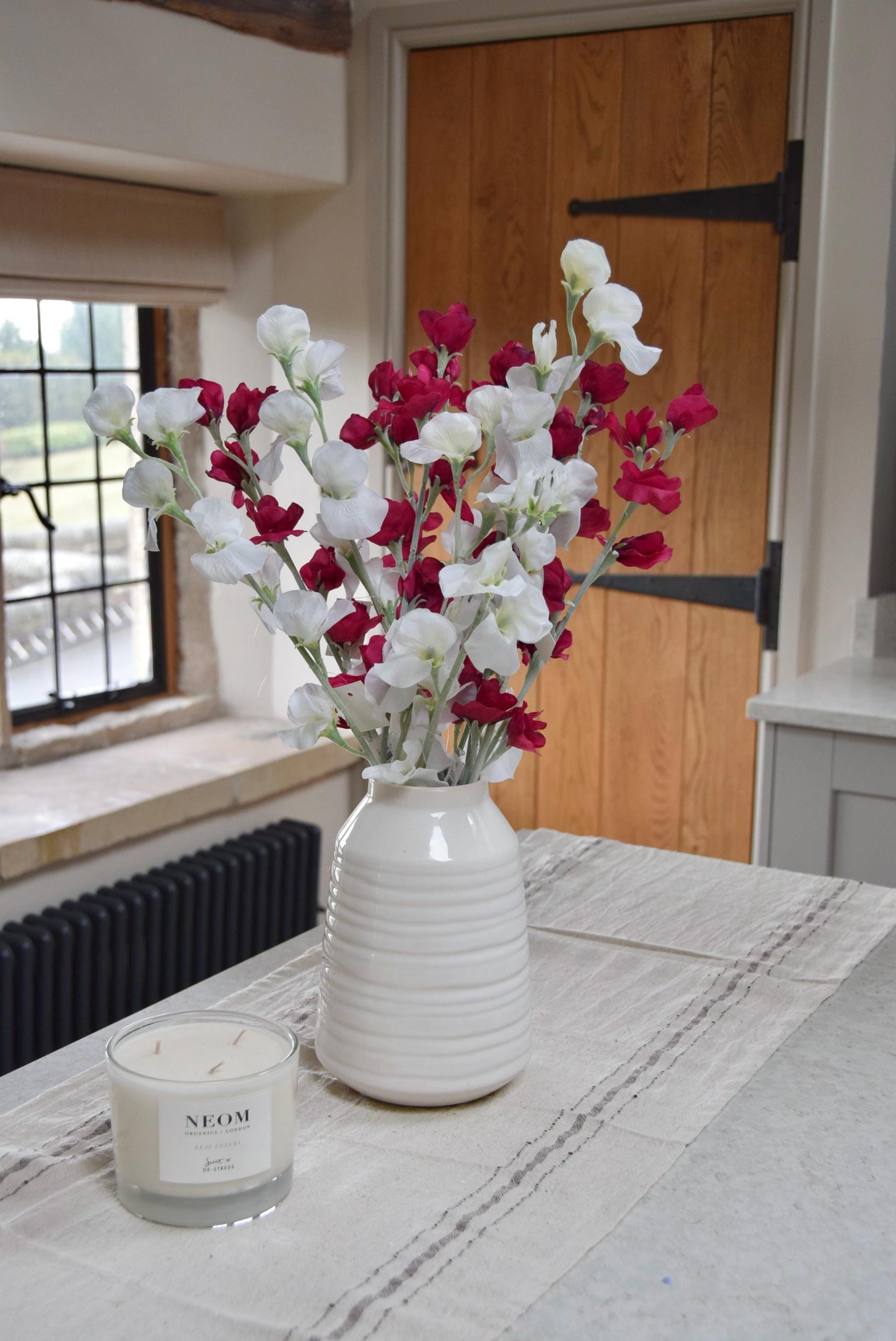 Red and white sweet peas set in a cream vase on a kitchen countertop in a country style kitchen for home decor.