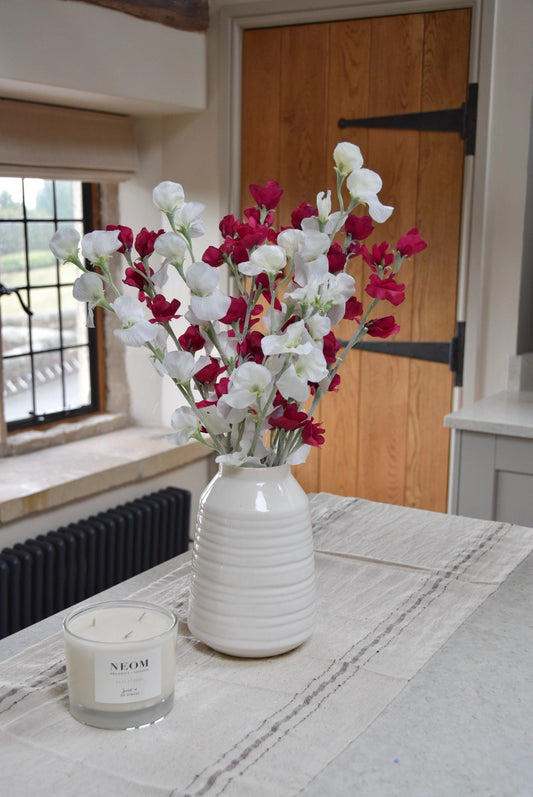 Red and white sweet peas set in a cream vase on a kitchen countertop in a country style kitchen for home decor.