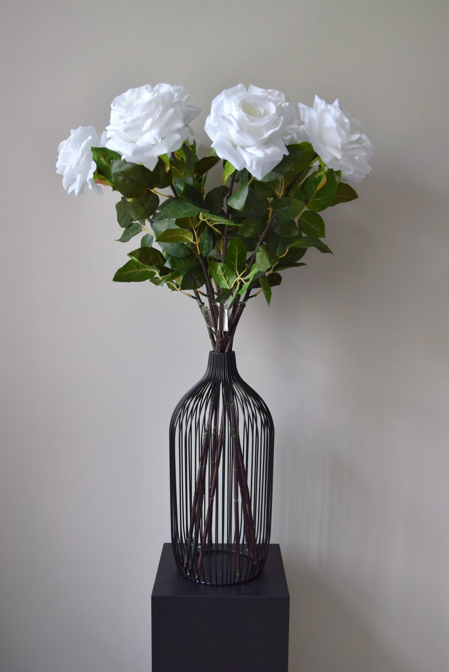 Tall white roses displayed in a black vase against a neutral background.