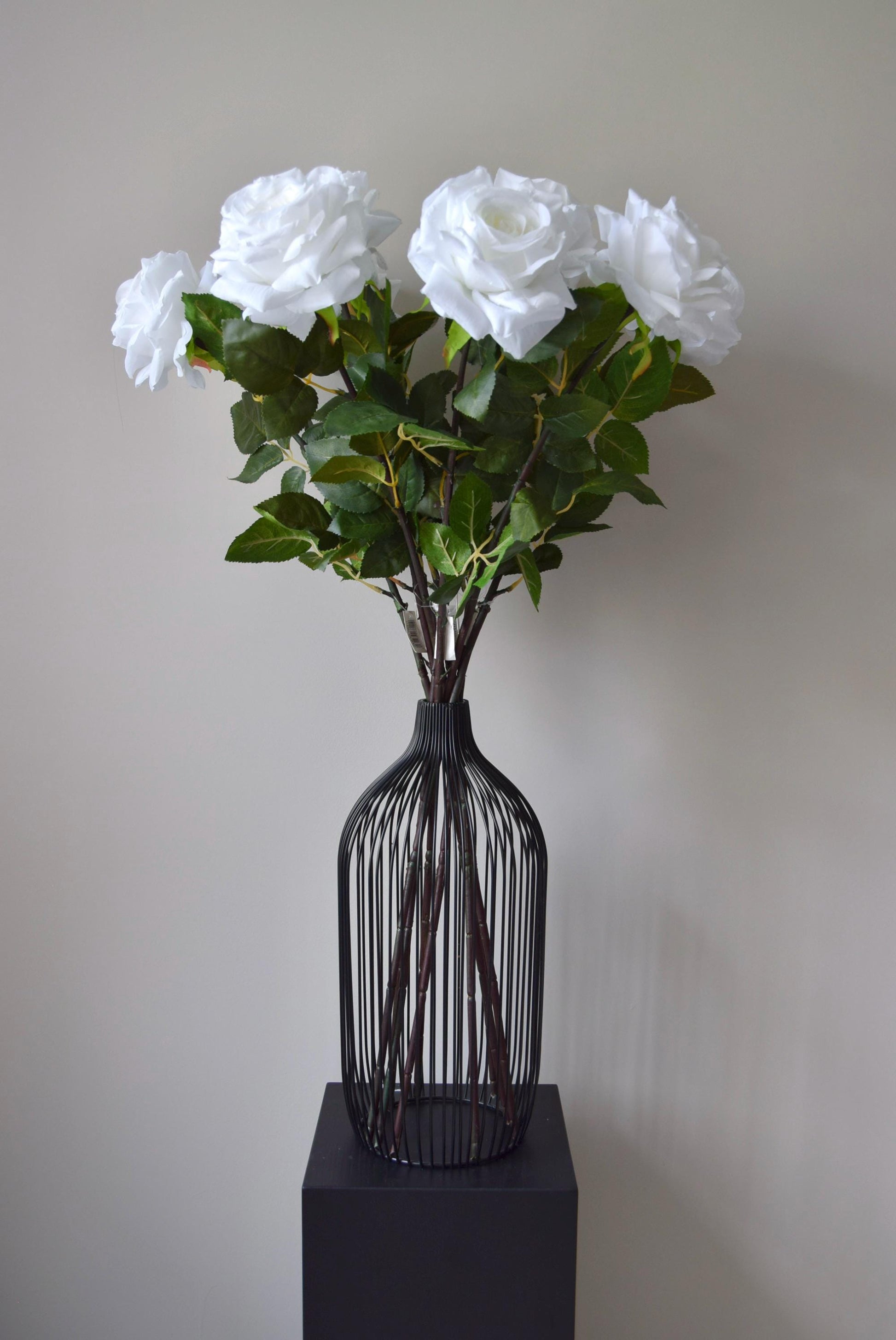 Tall white roses displayed in a black vase against a neutral background.