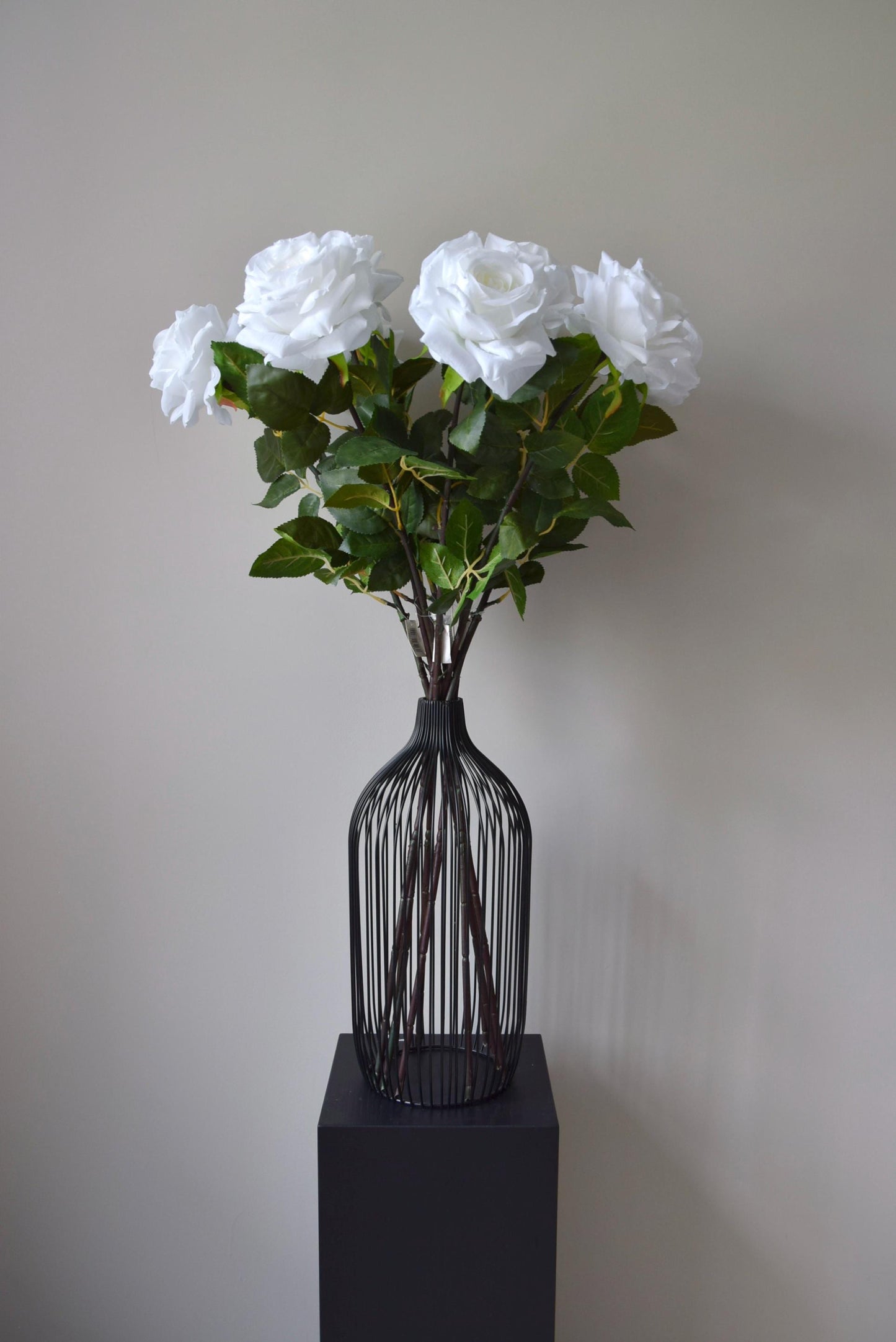 Tall white roses displayed in a black vase against a neutral background.