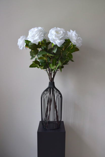 Tall white roses displayed in a black vase against a neutral background.